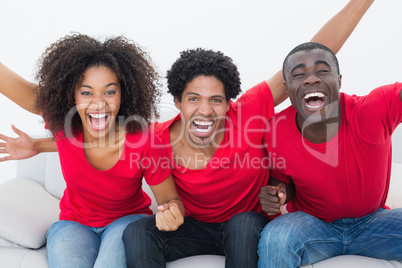 Football fans in red sitting on couch cheering