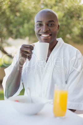 Handsome man in bathrobe having breakfast outside