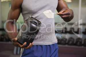 Body builder holding a scoop of protein mix in gym