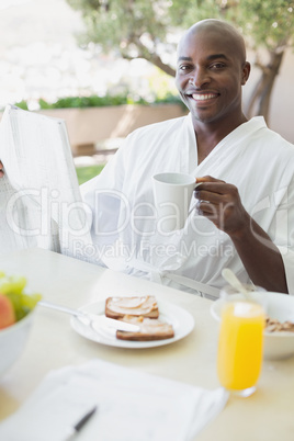 Handsome man in bathrobe having breakfast outside