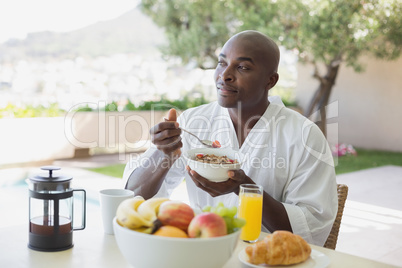 Handsome man in bathrobe having breakfast outside