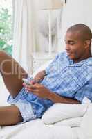 Happy man sitting on bed and texting on phone