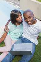Happy couple sitting in garden using laptop together