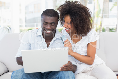 Attractive couple using laptop together on sofa to shop online