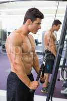 Shirtless muscular man using triceps pull down in gym