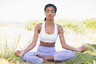 Fit woman sitting on grass in lotus pose with eyes closed