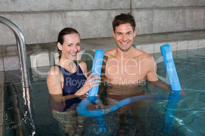 Happy couple holding foam rollers smiling at camera