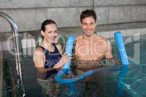 Happy couple holding foam rollers smiling at camera