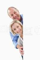 Mature couple smiling behind wall