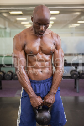 Muscular man lifting kettle bell in gym