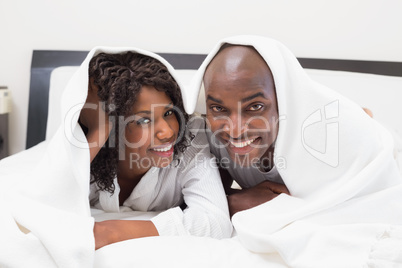 Happy couple lying on bed together under the duvet