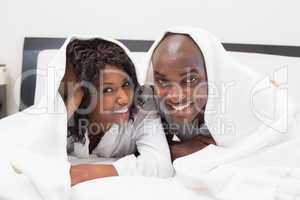 Happy couple lying on bed together under the duvet