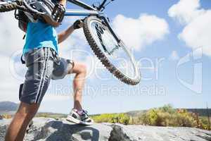 Fit man walking up rocky terrain holding mountain bike