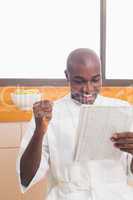 Happy man in bathrobe reading newspaper