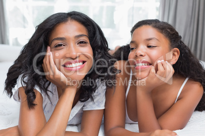 Pretty woman lying on bed with her daughter smiling at camera