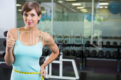 Fit brunette smiling at camera with measuring tape around waist