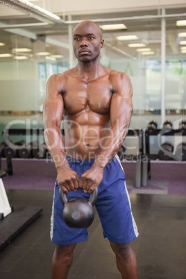 Muscular man lifting kettle bell in gym