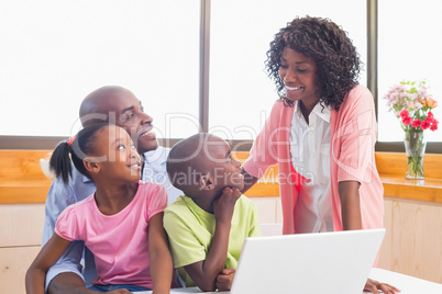 Cute siblings using laptop together with parents