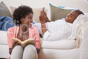 Happy couple relaxing together reading book and using smartphone