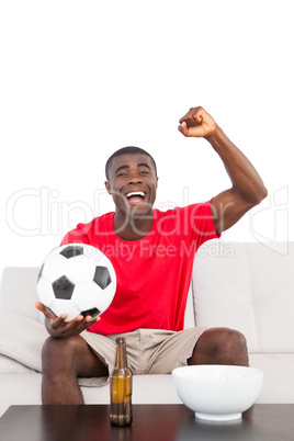 Football fan in red jersey sitting on couch cheering