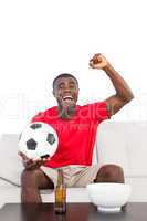 Football fan in red jersey sitting on couch cheering