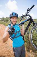 Fit man walking down trail holding mountain bike smiling at came