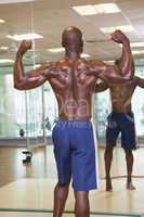 Rear view of muscular man flexing muscles in gym