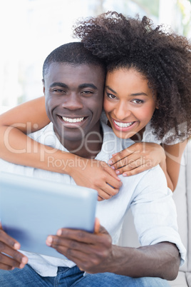 Attractive couple sitting on couch together looking at tablet