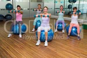 Fitness class holding dumbbells on exercise balls in studio