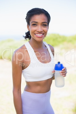 Fit woman holding sports bottle smiling at camera