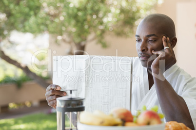 Man in bathrobe reading paper and having breakfast on terrace
