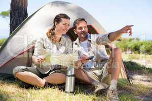 Outdoorsy couple looking at the map and pointing outside tent