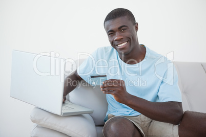 Casual man sitting on sofa using laptop to shop online