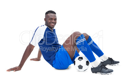 Football player in blue sitting with ball