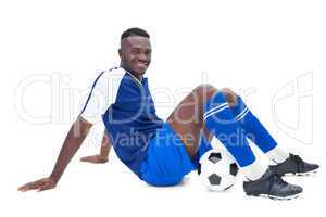 Football player in blue sitting with ball