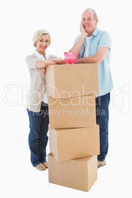 Older couple smiling at camera with moving boxes and piggy bank