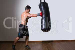 Shirtless muscular boxer with punching bag in gym