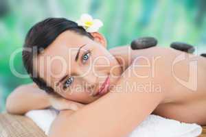 Beautiful brunette enjoying a hot stone massage smiling at camer