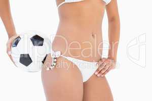 Athletic girl in white bikini holding football mid section