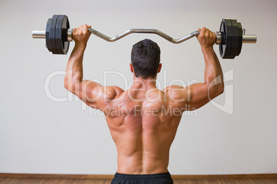 Shirtless muscular man lifting barbell in gym