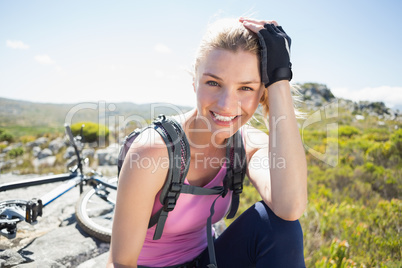 Fit pretty cyclist taking a break on rocky peak smiling at camer