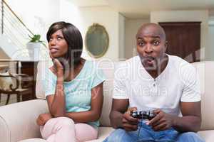 Bored woman sitting next to her boyfriend playing video games