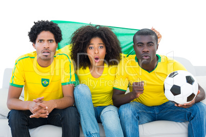 Excited football fans in yellow sitting on couch with brazil fla