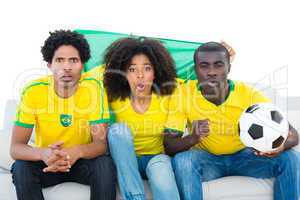 Excited football fans in yellow sitting on couch with brazil fla