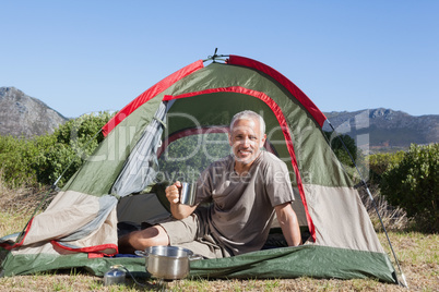 Happy camper holding mug outside his tent