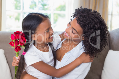 Pretty mother sitting on the couch with her daughter holding ros