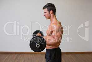 Shirtless muscular man lifting barbell in gym