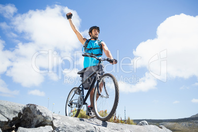 Fit man cycling on rocky terrain and cheering