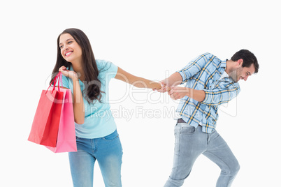 Attractive young man pulling his shopaholic girlfriend