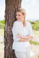 Attractive happy blonde standing by tree